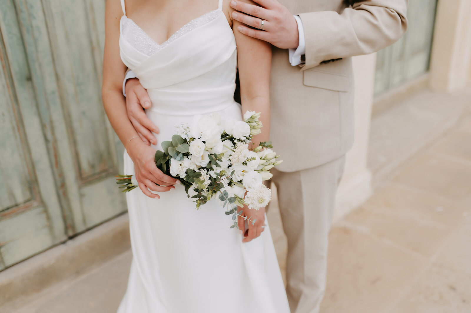Newlyweds holding a bouquet, photographed from the shoulders down