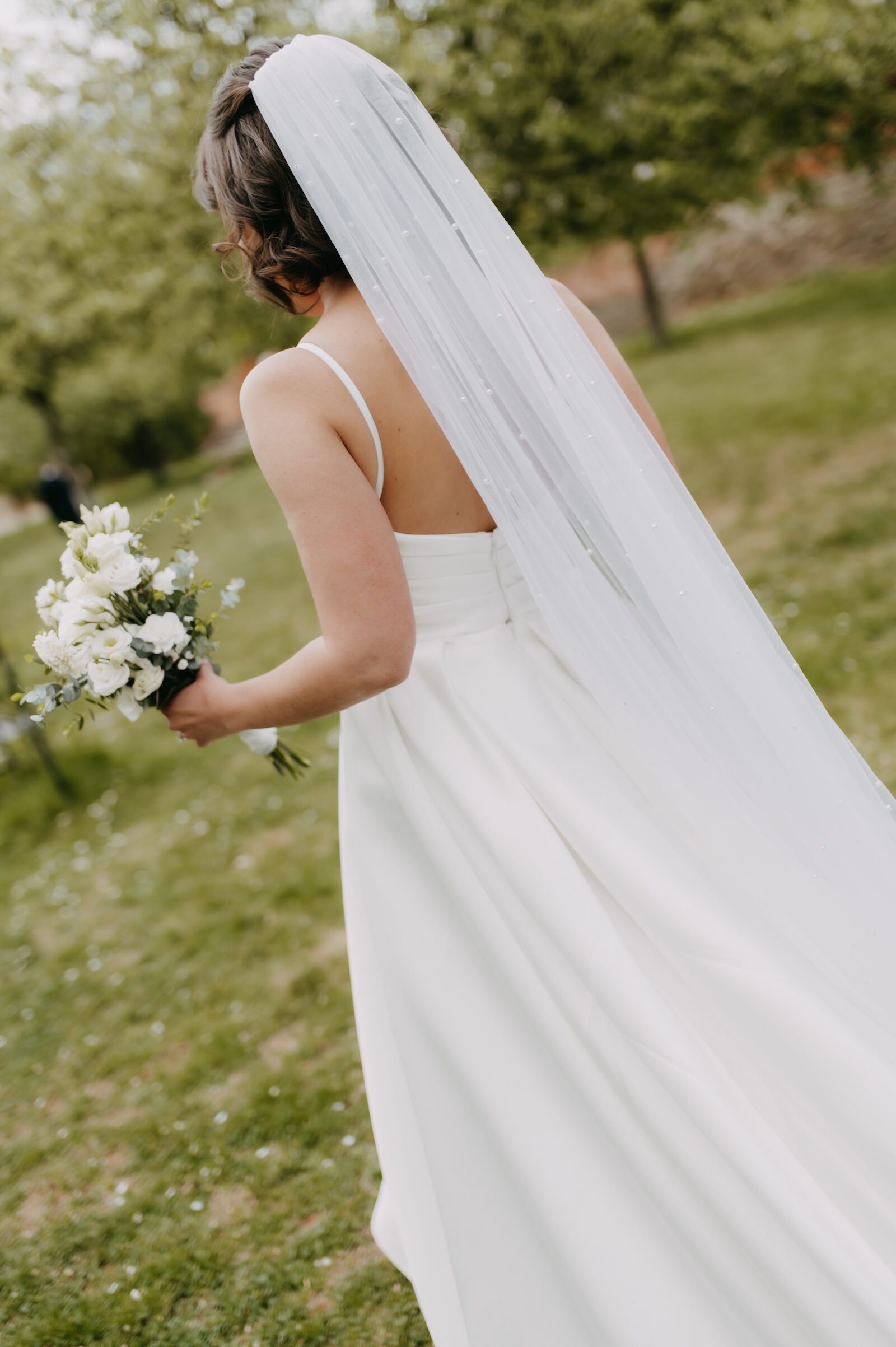 Bride from behind with a long pearl veil in an orchard